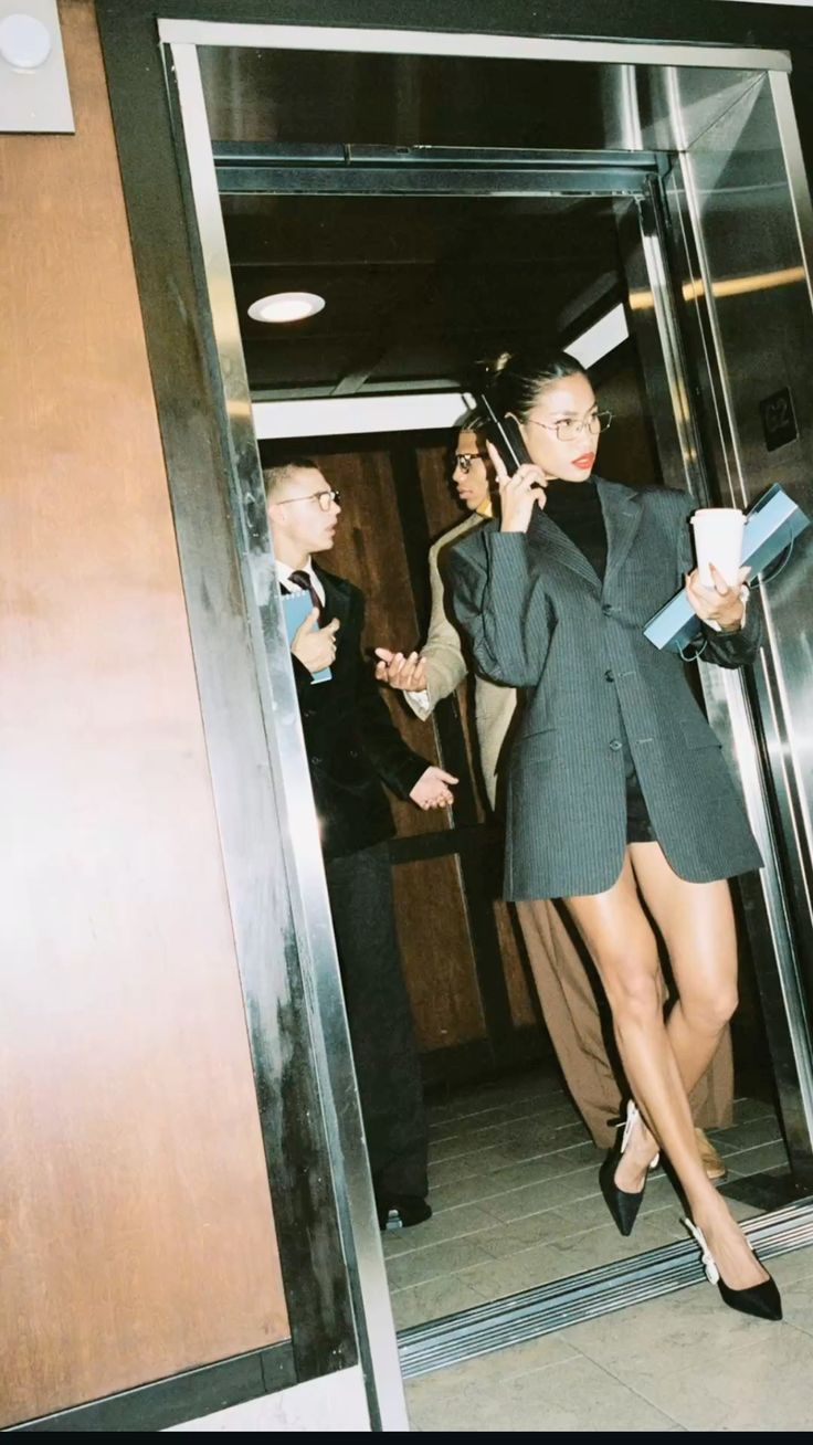 A woman stepping out of an office elevator carrying folders and coffee