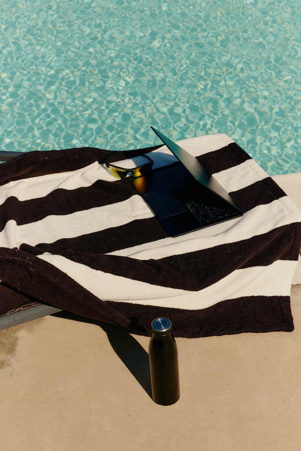 A laptop resting on a striped towel beside a pool